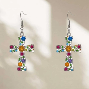 Detalle de pendientes en forma de cruz con coloridos motivos florales sobre blanco