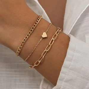 Close-up of three-piece gold chain bracelet set featuring heart charm and paperclip link