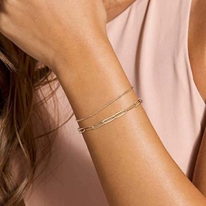 Close-up of gold paperclip chain and bead bracelets stacked on a woman's wrist
