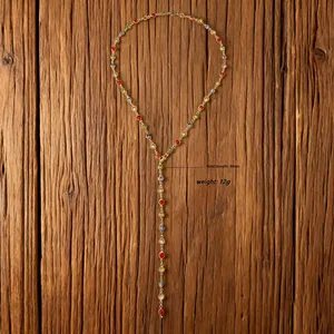 Detalle de collar en Y dorado de 80 cm con gemas de colores sobre fondo de madera