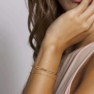 Close-up of bohemian gold layered bracelets featuring paperclip and satellite chain designs