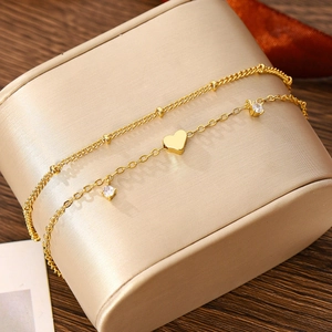 Detail of bohemian gold-layered chain bracelet with heart pendant and white zircon stones