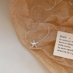 Macro shot of silver starfish pendant necklace on textured brown craft paper