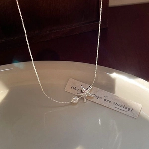 Elegant starfish necklace with silver star pendant and pearl on white ceramic plate