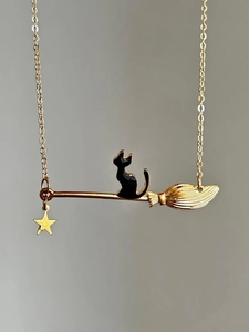 Dettaglio di una collana vintage con gatto in smalto nero seduto su una scopa dorata
