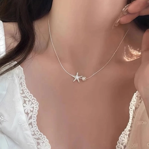 Close-up of a silver starfish pendant necklace with a pearl on a woman's collarbone