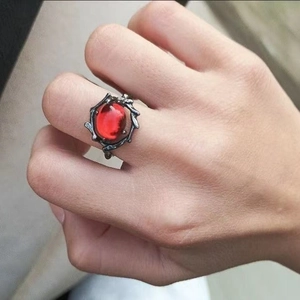 Primer plano detallado de un anillo gótico plateado con gema roja y textura de espinas