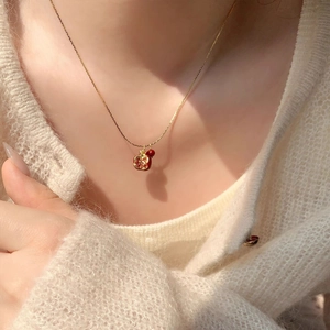 Dettaglio di una collana dorata con pendente a melograno su un maglione di maglia