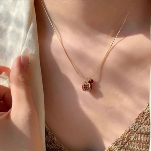 Dettaglio di una collana con ciondolo a melograno dorato e perline rosse su una modella