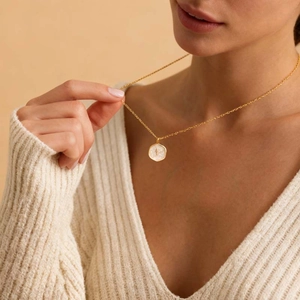 Close-up of a golden hexagonal pendant with a shell texture and a cross on a gold chain
