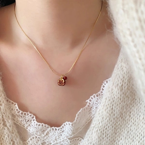 Dettaglio di una collana dorata con ciondolo a melagrana su sfondo di maglione bianco