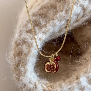 Collana con ciondolo a melograno vintage dorata e rosso scuro su fondo di lana morbida