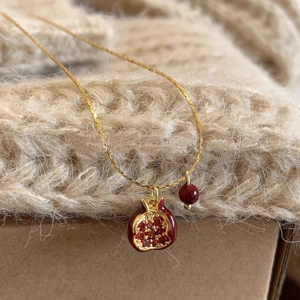 Dettaglio macro della collana di melograno rosso con smalto e catena dorata su maglione
