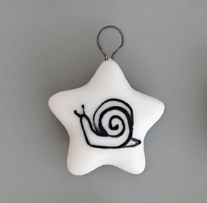 Detail of star-shaped white ceramic pendant with a hand-painted black snail and gold loop