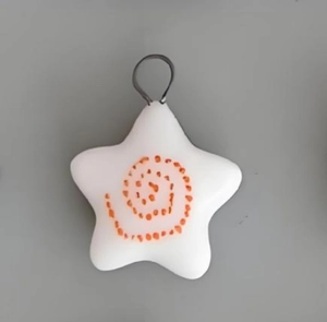 Close-up of a white star-shaped pendant with orange spiral texture and silver ring clasp