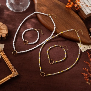 Détail du collier de perles avec pendentifs dorés sur un fond de tissu texturé