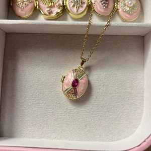 Vista macro de un relicario de corazón en oro de 18K con esmalte rosa y gema roja