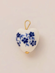 Makroaufnahme eines Herz-Porzellananhängers mit blauem Blumenmuster und Goldöse