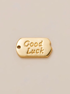 Detail of a rectangular gold-plated charm featuring engraved Good Luck text and textured edges