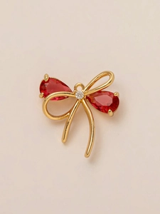 Macro detail of 18K gold-plated bow charm with pear-shaped red gemstones and small white diamond