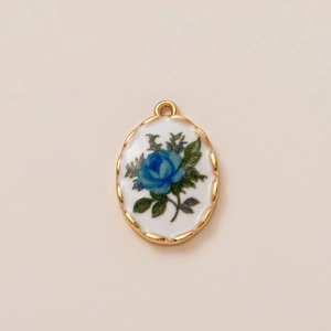 Macro di un ciondolo ovale placcato oro con rosa blu smaltata e design floreale vintage