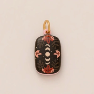 Detail of a rectangular black ceramic pendant with pink floral art and moon phase patterns