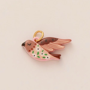 Detailed close-up of a pink bird pendant with delicate flower patterns and gold ring
