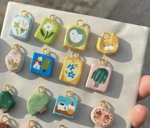 Close-up of handmade 18K gold-plated clay pendants featuring colorful cartoon patterns