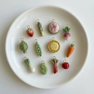 Artisanal ceramic fruit and vegetable pendants with 18K gold plated loops on a white plate