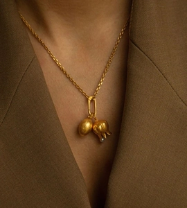 Dettaglio della collana dorata con ciondoli a forma di seme e tulipano su collo