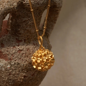 Macro di un ciondolo a sfera cava placcato oro 18K con dettagli floreali opachi