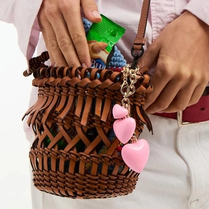 Detail of pink heart charms on a brown woven leather bucket bag with fringe trim
