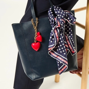 Close-up of heart charms and polka dot silk scarf on a blue leather tote bag