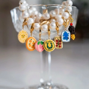 Elegantes Perlenarmband mit bunten Emaille-Anhängern an einem Glasrand