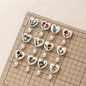 Dettaglio di perline in ceramica a forma di cuore con motivi floreali e catena dorata