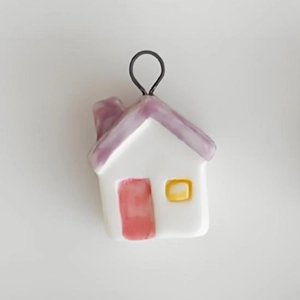 Detail view of a white ceramic house pendant with purple roof and golden hanger