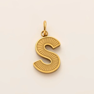 Detailed macro of a 18K gold-plated letter S pendant with textured sunburst engraving