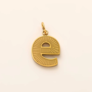 Close-up of golden letter E pendant featuring intricate vertical and radial textures