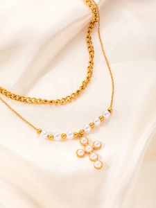 Dettaglio di una collana a due strati in titanio dorato con ciondolo a croce di perle