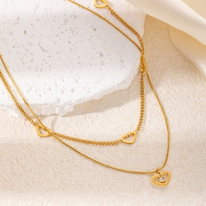 Dettaglio di una collana dorata a due strati con ciondoli a cuore su marmo