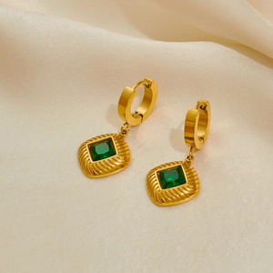 Detail of vintage gold earrings with emerald green square stones on beige silk fabric