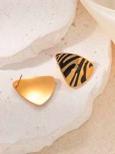 Close-up of golden triangle earrings with black animal print on a stone pedestal