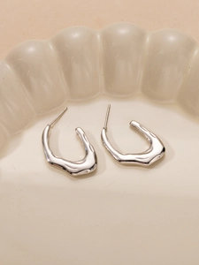 Macro di orecchini irregolari in argento su un piatto di ceramica con bordi ondulati