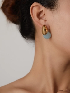 Detail of elegant gold teardrop earrings with translucent blue resin bead charm on ear