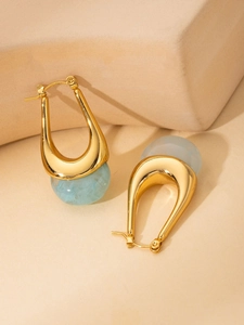 Detail of gold U-shaped hoop earrings with light blue marble resin beads on stone