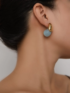 Close-up of minimalist gold plated teardrop earring with light blue resin on model