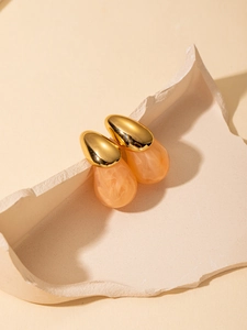 Close-up of golden titanium earrings with amber resin teardrop pendants on stone