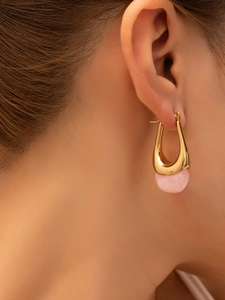 Close-up of a U-shaped gold earrings with pink stone pendant worn on a model earlobe