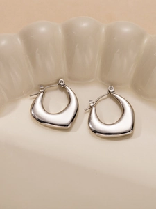 Orecchini a cerchio irregolari in argento lucido con design curvo spesso su piatto ceramico