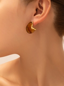 Detail view of gold wavy earrings with amber resin texture on model's ear